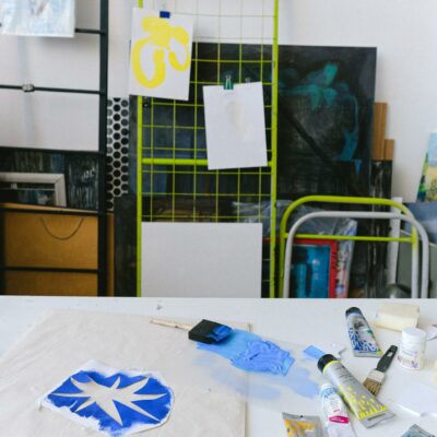 Bag with blue print placed on white table with paintbrush and set of tubes for painting in creative workshop with paintings
